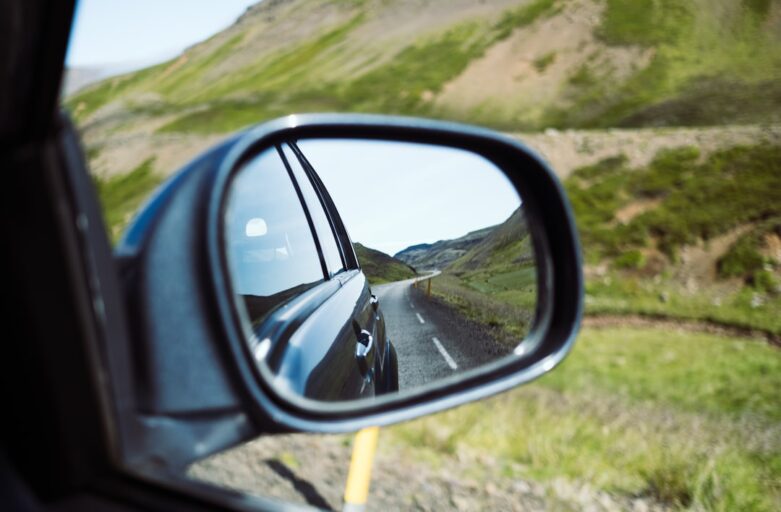 Close-up shot of a car's rearview mirror, with the road behind in sharp focus and the road ahead blurred, symbolizing the ...