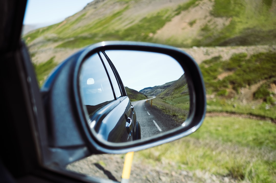 Close-up shot of a car's rearview mirror, with the road behind in sharp focus and the road ahead blurred, symbolizing the ...