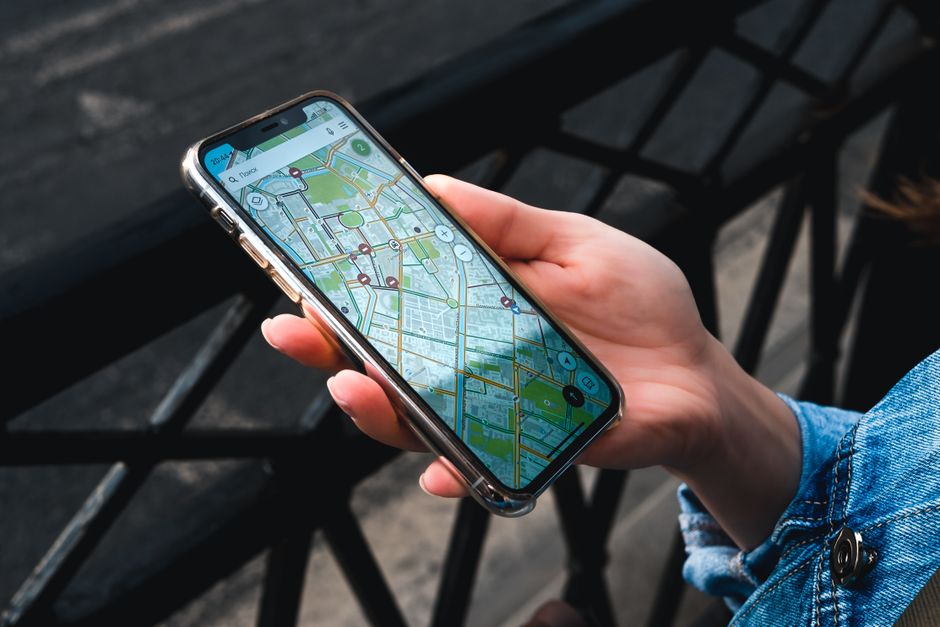 A close-up shot of a person holding a smartphone displaying a map application with location pins for local businesses, set against a bright, clean background.