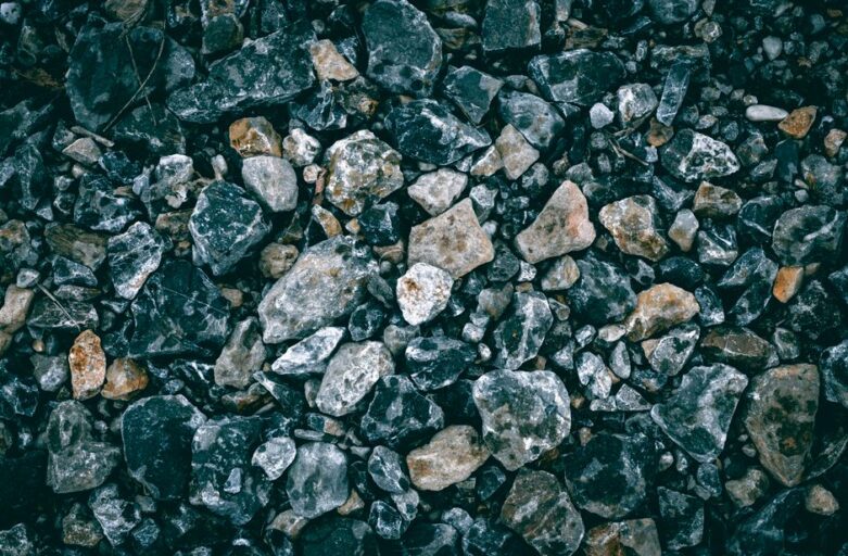 Close-up, minimalist photo of a single, gleaming gold rock resting among a bed of plain grey stones, symbolizing finding v...
