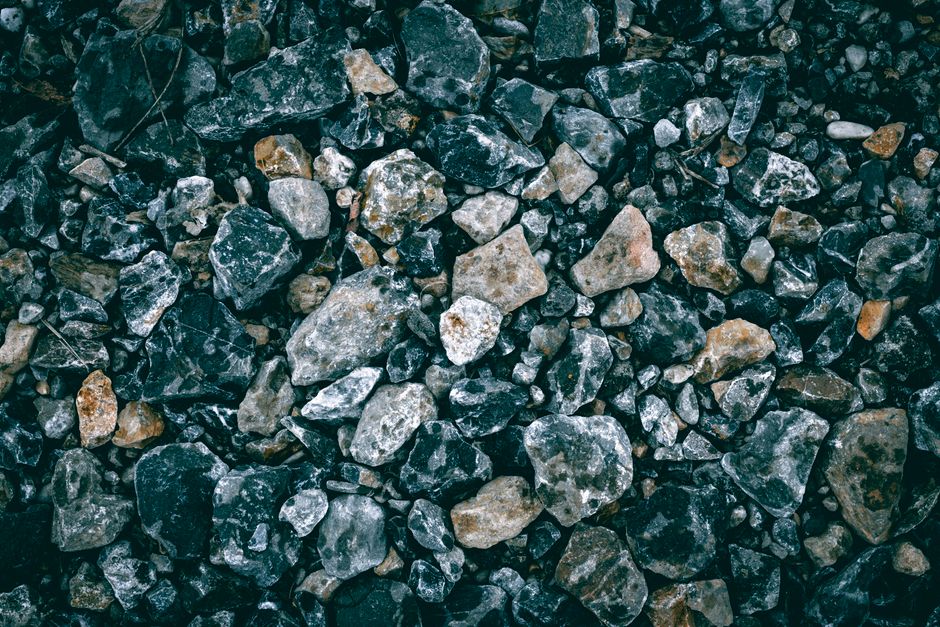 Close-up, minimalist photo of a single, gleaming gold rock resting among a bed of plain grey stones, symbolizing finding v...