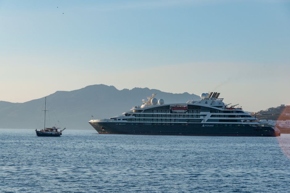 A small, agile sailboat navigating the ocean beside a massive cruise ship, illustrating the concept of a boutique firm competing with a large corporation.